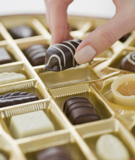 Woman holding chocolate over box of chocolates.