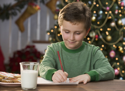 Boy writing letter in front of Christmas tree.