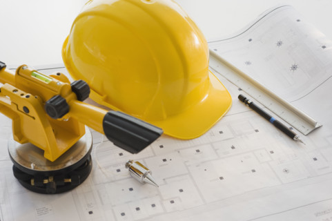 Hard hat and surveying equipment on blueprints.