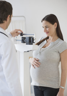 Pregnant Hispanic woman on scale in doctor’s office.