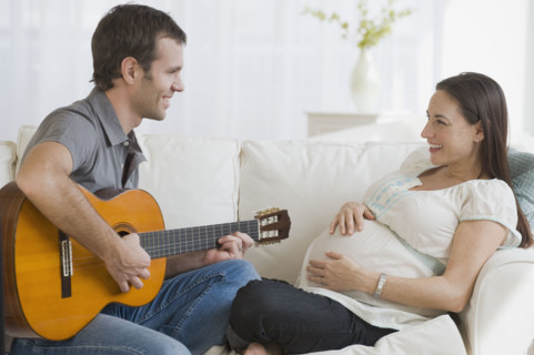 Hispanic man playing guitar for pregnant wife.