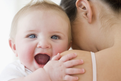Baby laughing over mother’s shoulder. Date : 2008