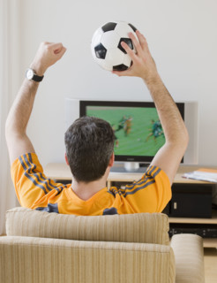Man with soccer ball cheering at television.