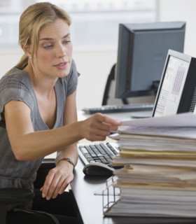 Businesswoman with stack of paperwork on desk.