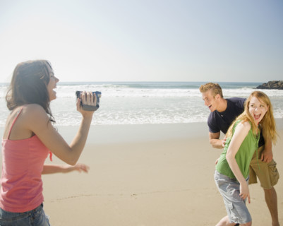 Woman video recording friends at beach. Date : 2008