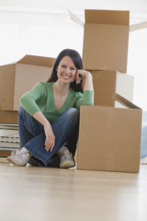 Woman leaning on moving box in new house.