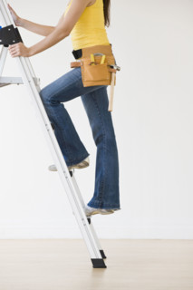 Woman wearing tool belt climbing ladder.