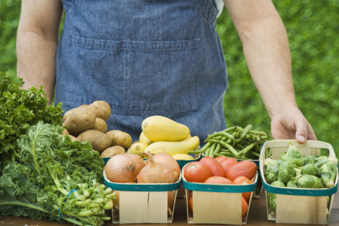 Farmer next to baskets of vegetables.