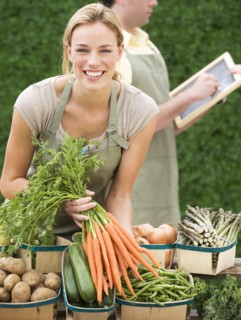 Woman next to baskets of vegetables.