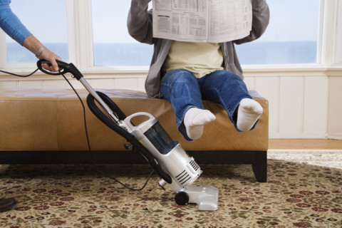 Woman vacuuming under man’s feet. Date : 2008