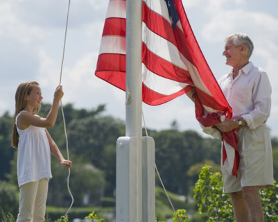 Grandfather and granddaughter raising American flag.