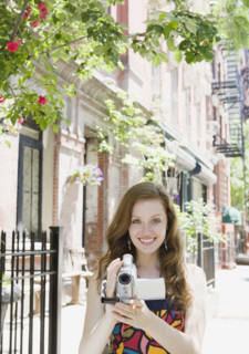 Woman holding video camera in urban setting. Date : 2008