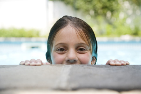 Girl peeking over edge of swimming pool. Date : 2008