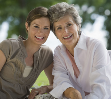 Mother and adult daughter posing outdoors.