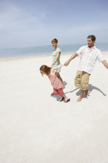 Girl holding hands with mother and father on beach. Date : 2008
