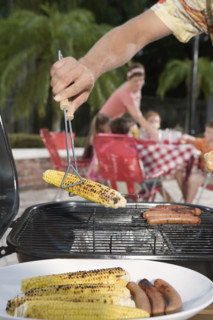 Man grilling hotdogs and corn in backyard. Date : 2008