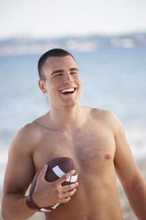 Young man holding football on beach. Date : 2008
