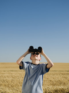Boy in field looking through binoculars . Date : 2008