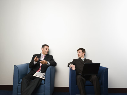 Businessmen sitting in chairs in office lobby. Date : 2008