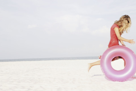 Teenage girl rolling inflatable ring on beach. Date : 2008