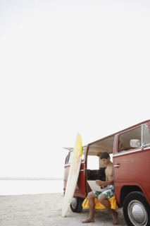 Young surfer using laptop in van on beach. Date : 2008