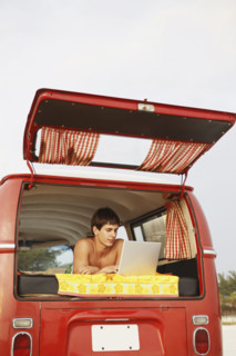 Young surfer using laptop in van on beach. Date : 2008