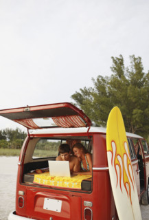 Young couple using laptop in van on beach. Date : 2008
