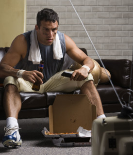 Football player watching game on sofa with beer. Date: 2008