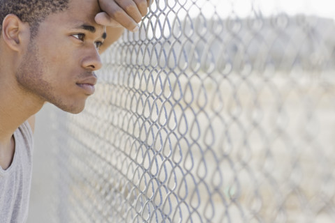 Young man leaning against chain-link fence. Date : 2008