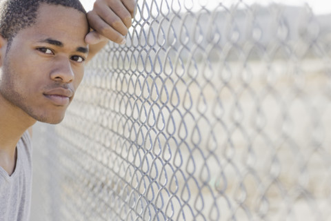 Portrait of young man leaning against chain-link fence. Date : 2008