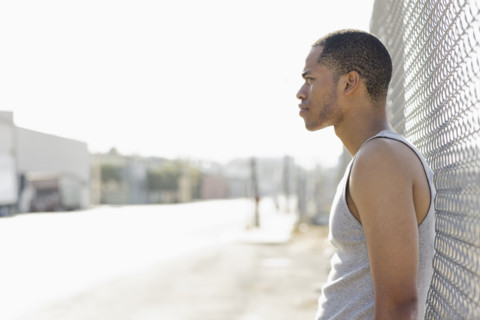 Young man leaning against chain-link fence. Date : 2008