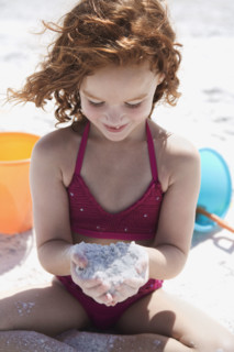 Girl in bikini cupping sand on beach. Date : 2008