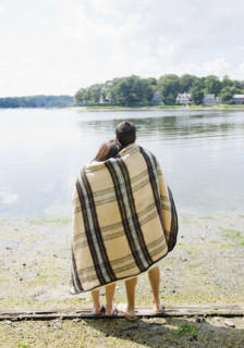 Couple wrapped in blanket looking out at lake. Date: 2008