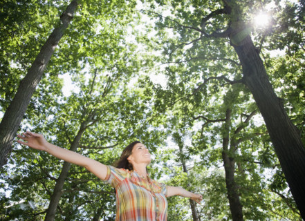 Woman standing below trees with arms outstretched. Date : 2008