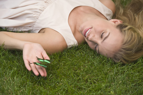 Woman laying on grass holding green butterfly.