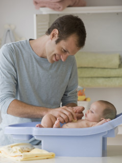 Father bathing baby son in baby bathtub.