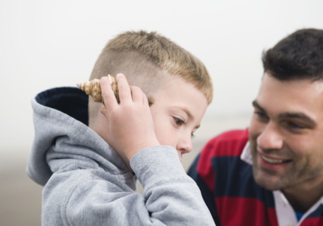 Father watching son hold seashell up to ear. Date : 2008