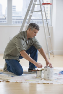 Man opening paint cans on drop cloth.