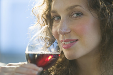 Close up portrait of woman smelling red wine.