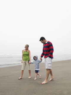 Parents holding hands with son on beach. Date : 2008