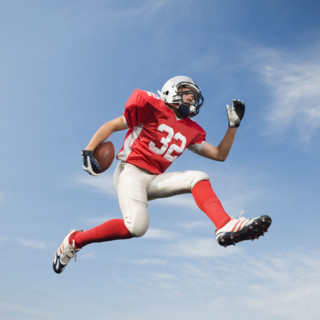 Football player in mid-air holding football. Date: 2008