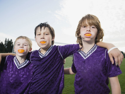 Portrait of boys in soccer uniforms with orange wedges in mouth. Date : 2008