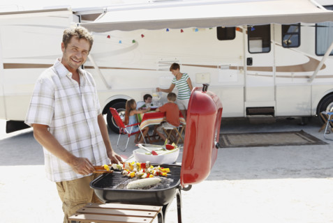 Man barbecuing with family and motor home in background. Date : 2008