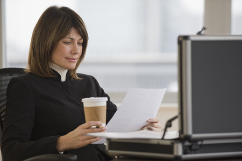 Businesswoman holding coffee and reading paperwork.