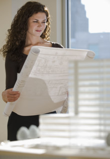 Architect viewing blueprints near building model.