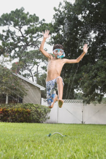 Boy with snorkeling mask running through sprinkler. Date : 2008