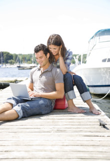 Couple using laptop on dock. Date : 2008