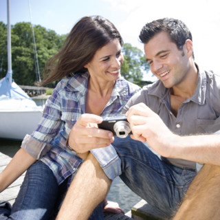 Couple sitting on dock looking at photos on digital camera. Date : 2008
