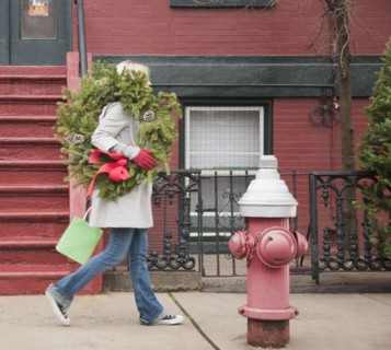 Woman carrying Christmas wreath on urban street. Photographe : Jamie Grill