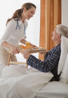 Nurse giving senior man breakfast.